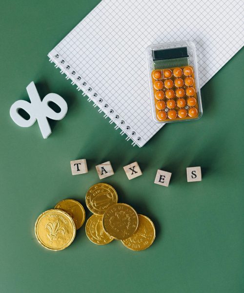 Flat lay of calculator, gold coins, notebook, and tax symbols on a green background.
