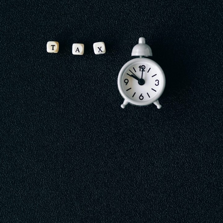 Miniature clock and word tax on black background symbolizing tax season deadlines.